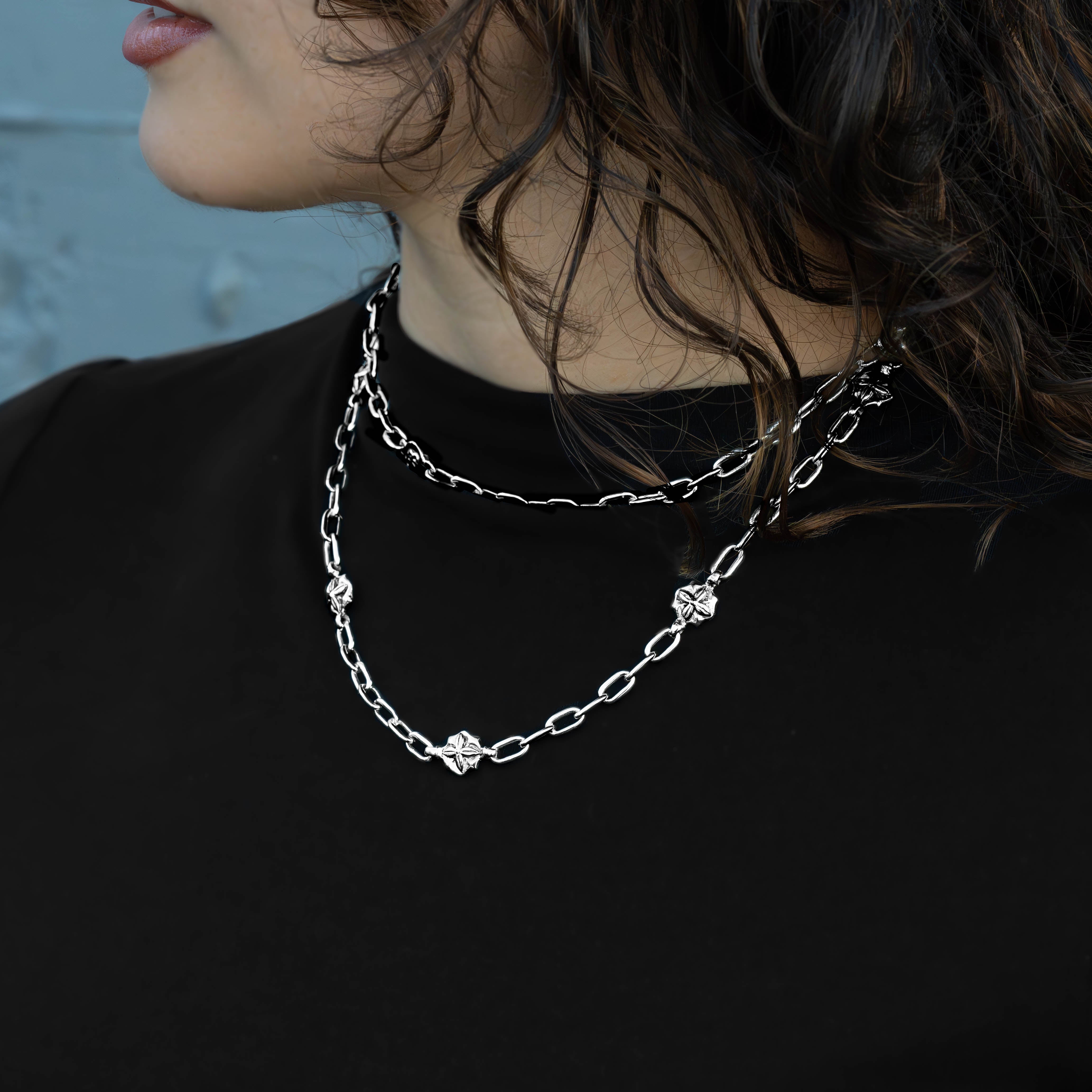 A close-up of a person wearing a layered silver chain necklace with small geometric and floral-like links over a black top.