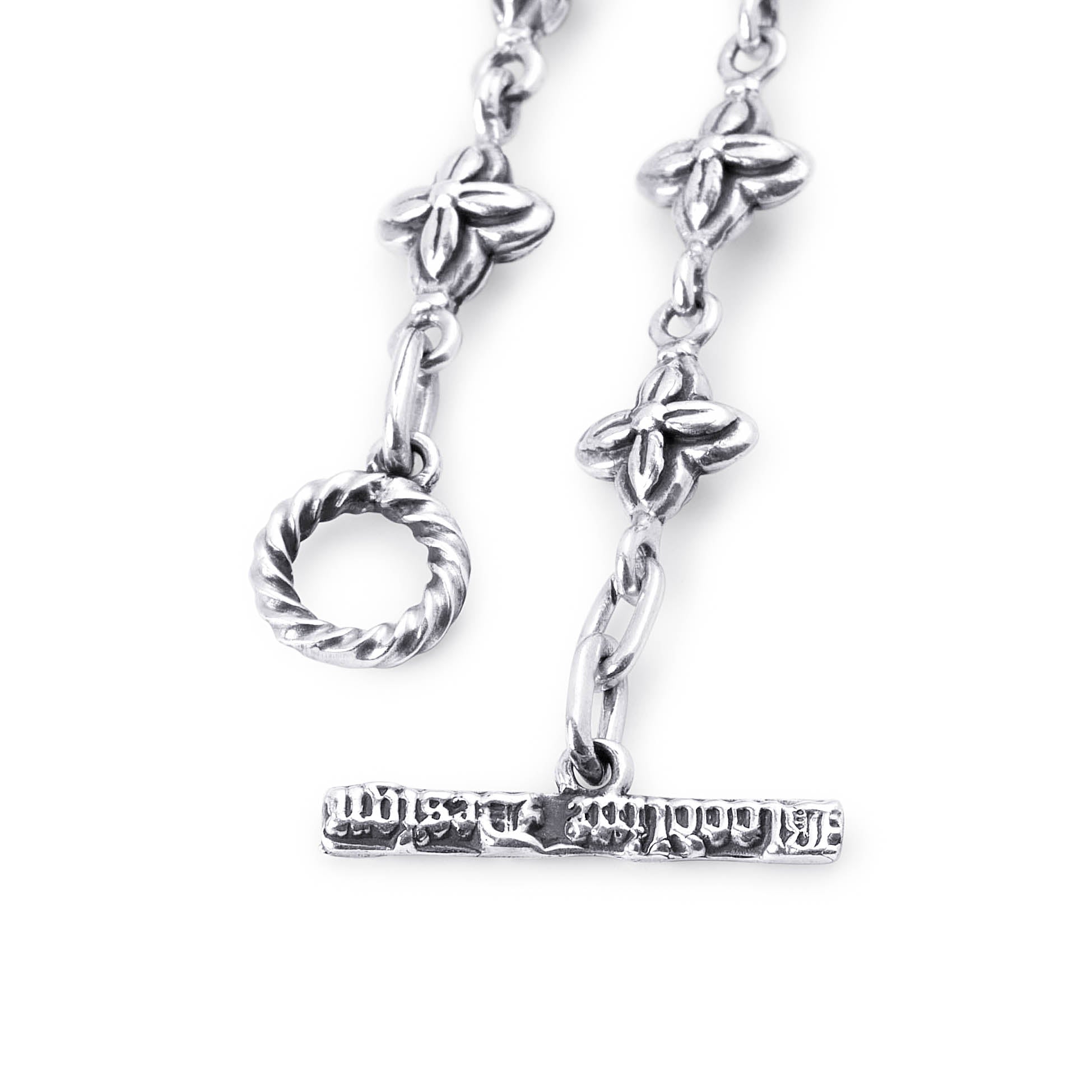 A close-up of a silver-toned jewelry piece featuring a twisted ring clasp, floral link details, and a horizontal bar with engraved text, shown on a plain white background.