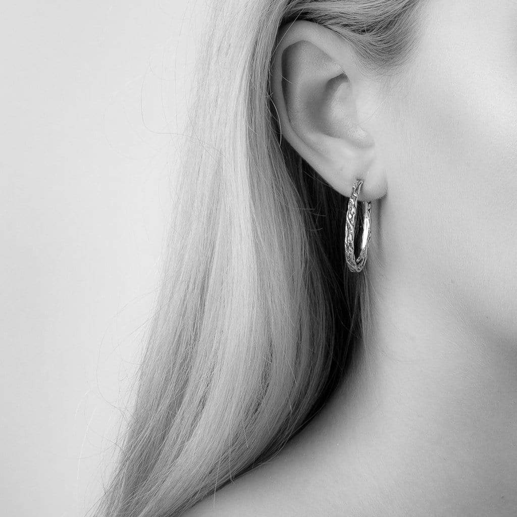 Medium sized oval shaped Solid sterling silver hoop stud with vine texture on model.