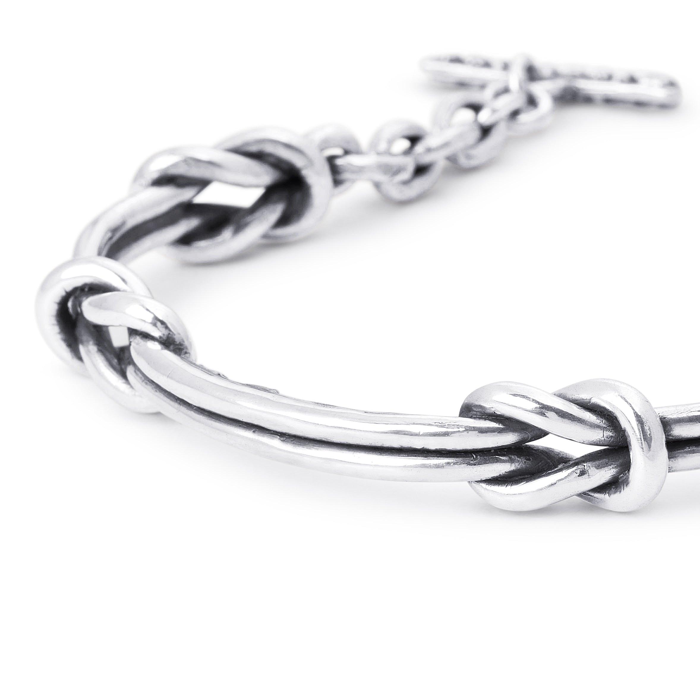A close-up of a polished silver-toned metal bracelet featuring a central knotted bar design, with a matching chain and toggle clasp visible against a clean white background.