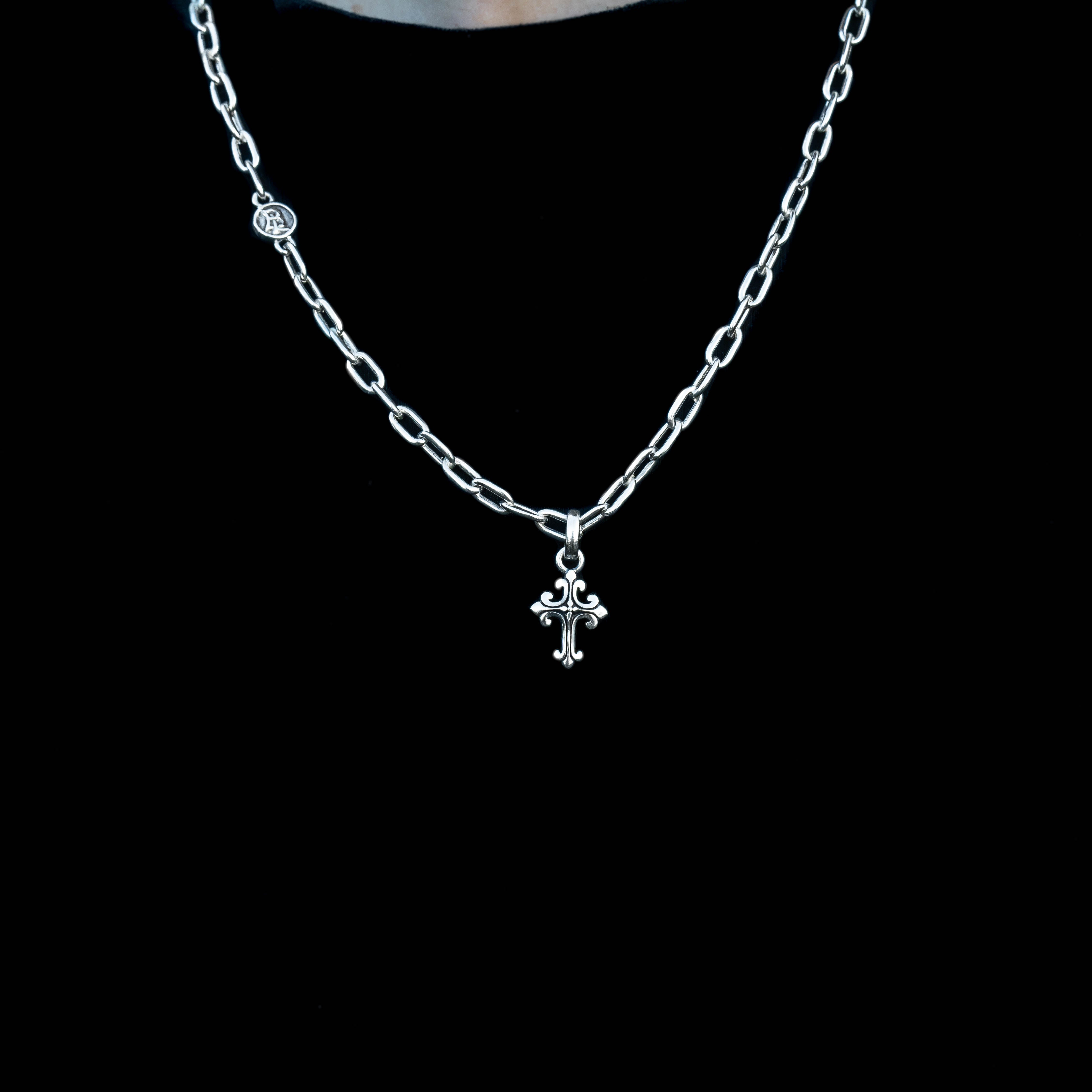 A silver chain necklace with a small cross pendant, displayed against a solid black background.