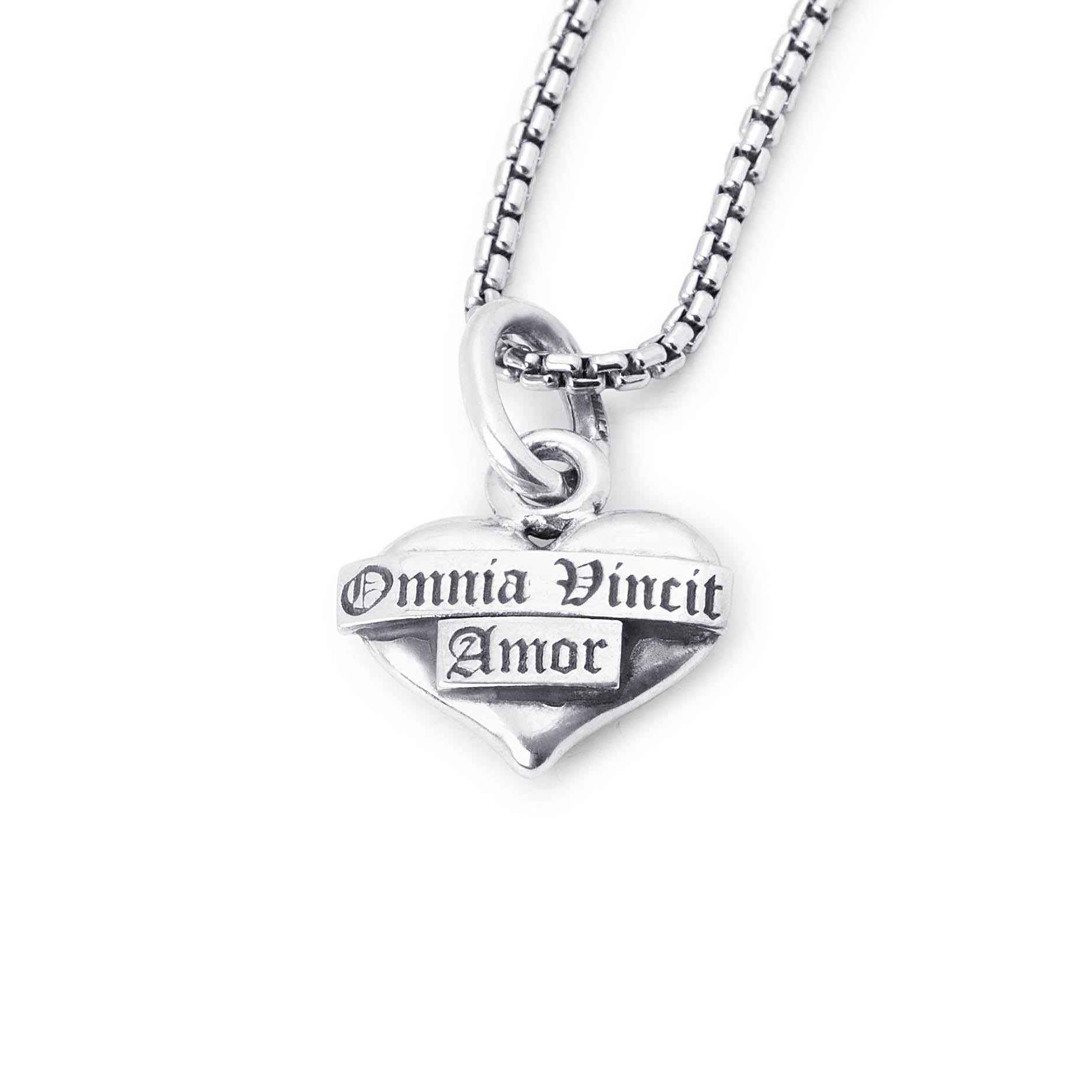 A silver heart pendant necklace engraved with the gothic text 'Omnia Vincit Amor' on a matching silver box chain, shown against a plain white background.