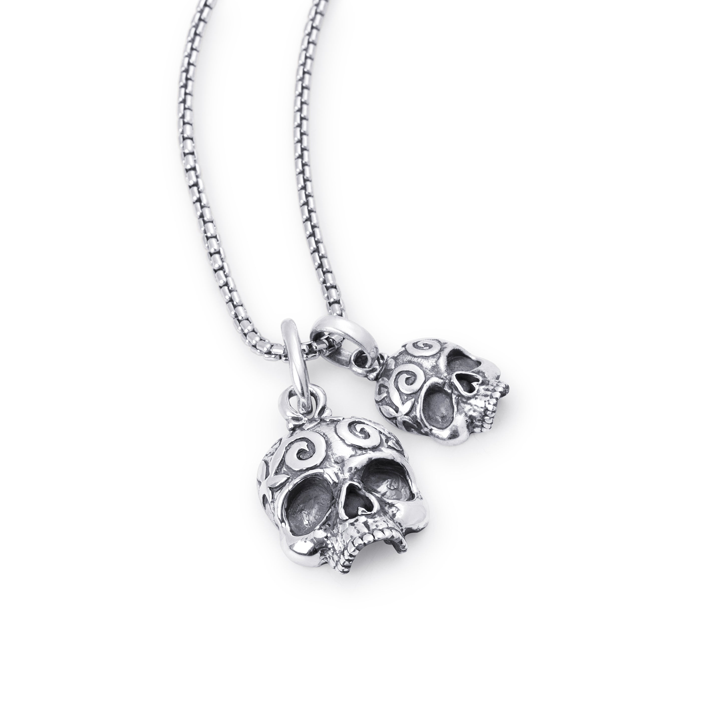 A silver-toned skull pendant necklace with an ornate scrollwork design, shown on a matching box chain against a plain white background.