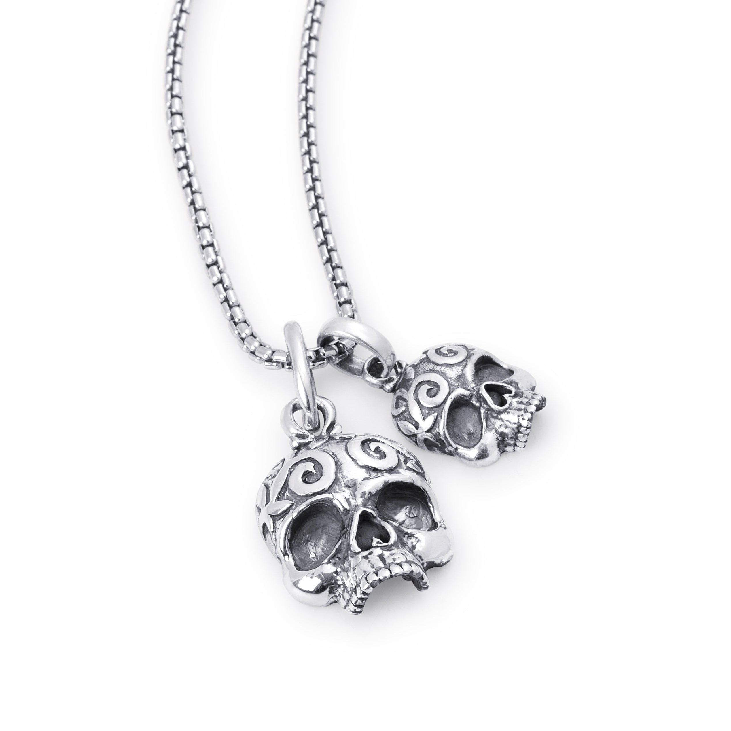 A silver-toned skull pendant necklace with an ornate scrollwork design, shown on a matching box chain against a plain white background.