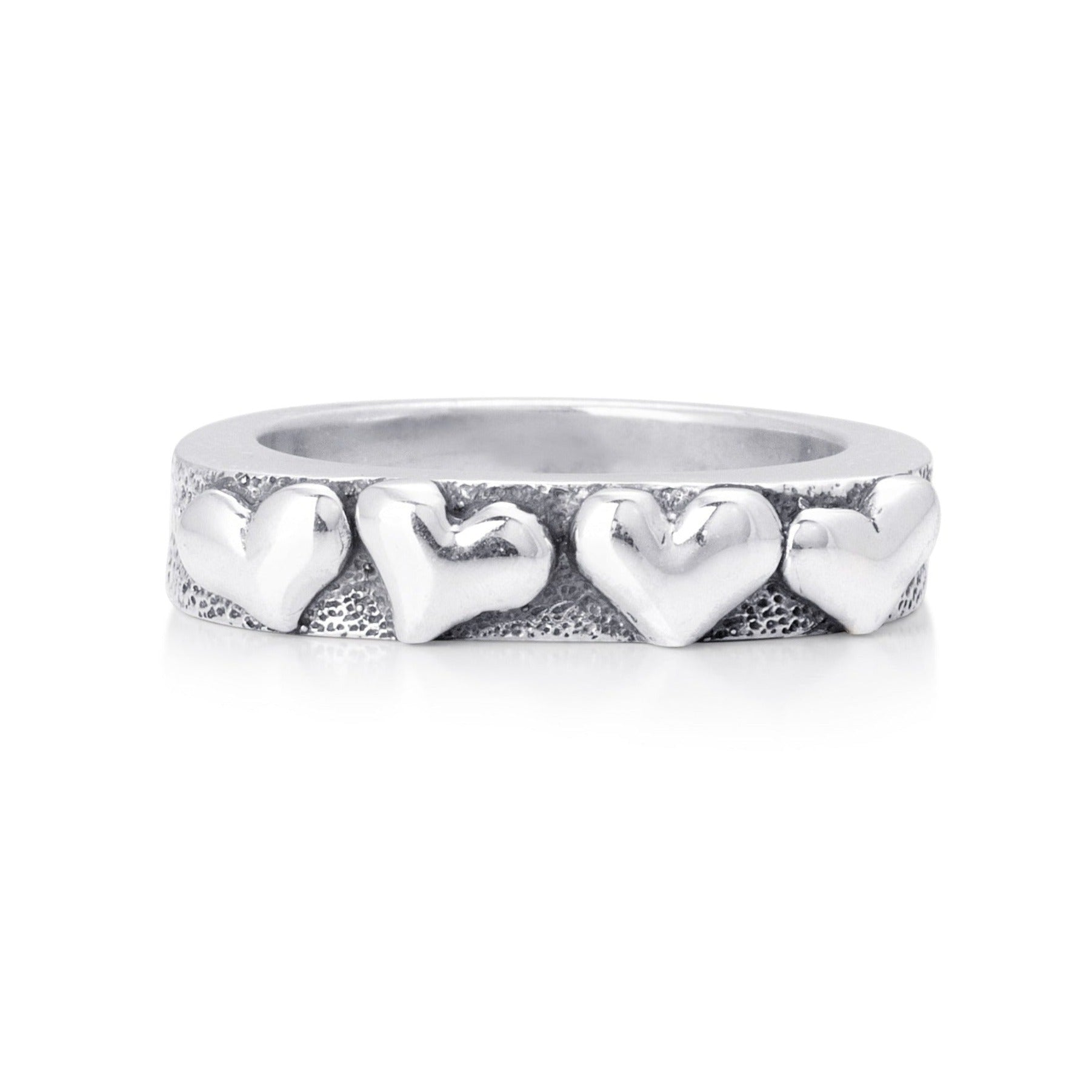 Solid sterling silver band with four hearts exposed on the top. Pitting surrounds the hearts on the top. Front view of the Ring